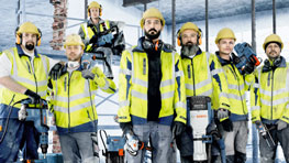 六名戴著黃色安全帽和警示背心的建築工人在工地上站著。