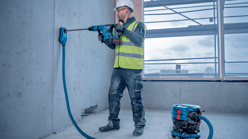 一個戴著頭盔和背心的男人正在鑽一面混凝土牆。