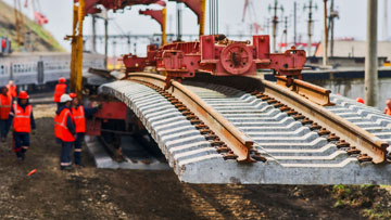 穿著橙色衣服的工人正在用起重機鋪設軌道。