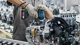 一名戴著安全帽和防護口罩的工人在腳手架上使用電鑽。