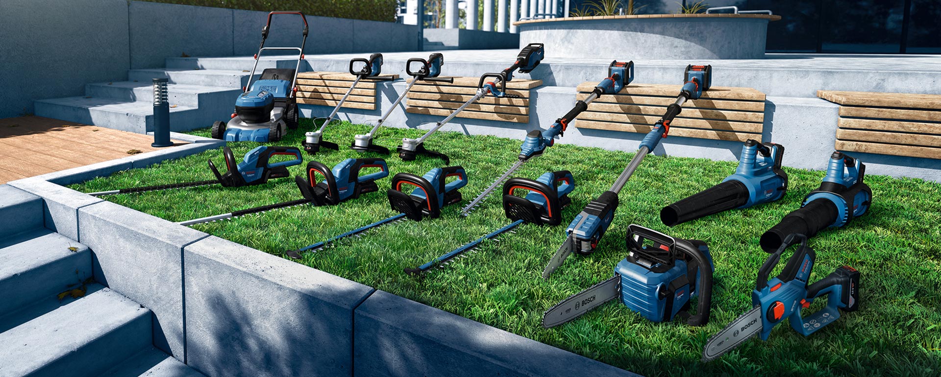 一組藍色園藝工具放在綠色草坪上，包括割草機、修剪機和吹葉機，周圍是灰色混凝土台階和木板。