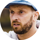 一個留著鬍子的男人戴著藍色的帽子，表情嚴肅。