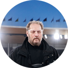 一個留著鬍子的男人穿著黑色夾克，站在聚光燈下。