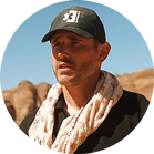 一個戴著黑色帽子和圍巾的男人站在岩石景觀前。