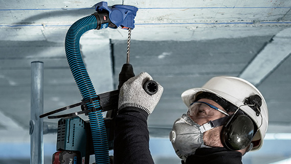 一名戴著安全帽和耳罩的工人在天花板上鑽孔。