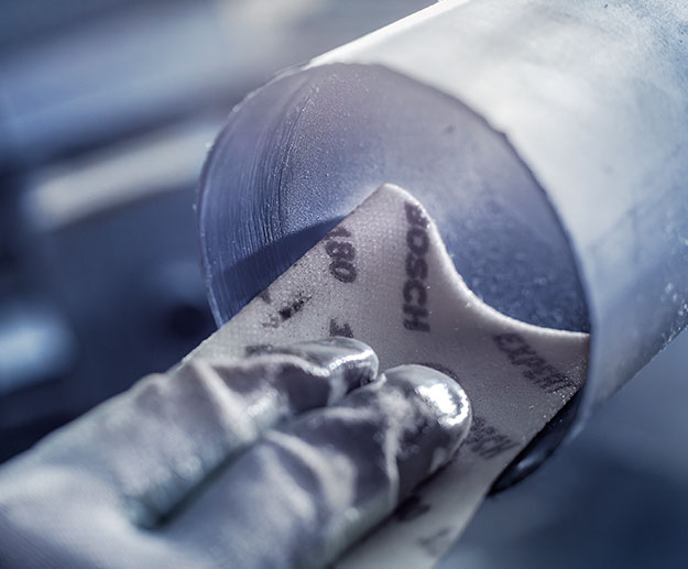 一隻手握著博世砂紙在一個圓形金屬件上。